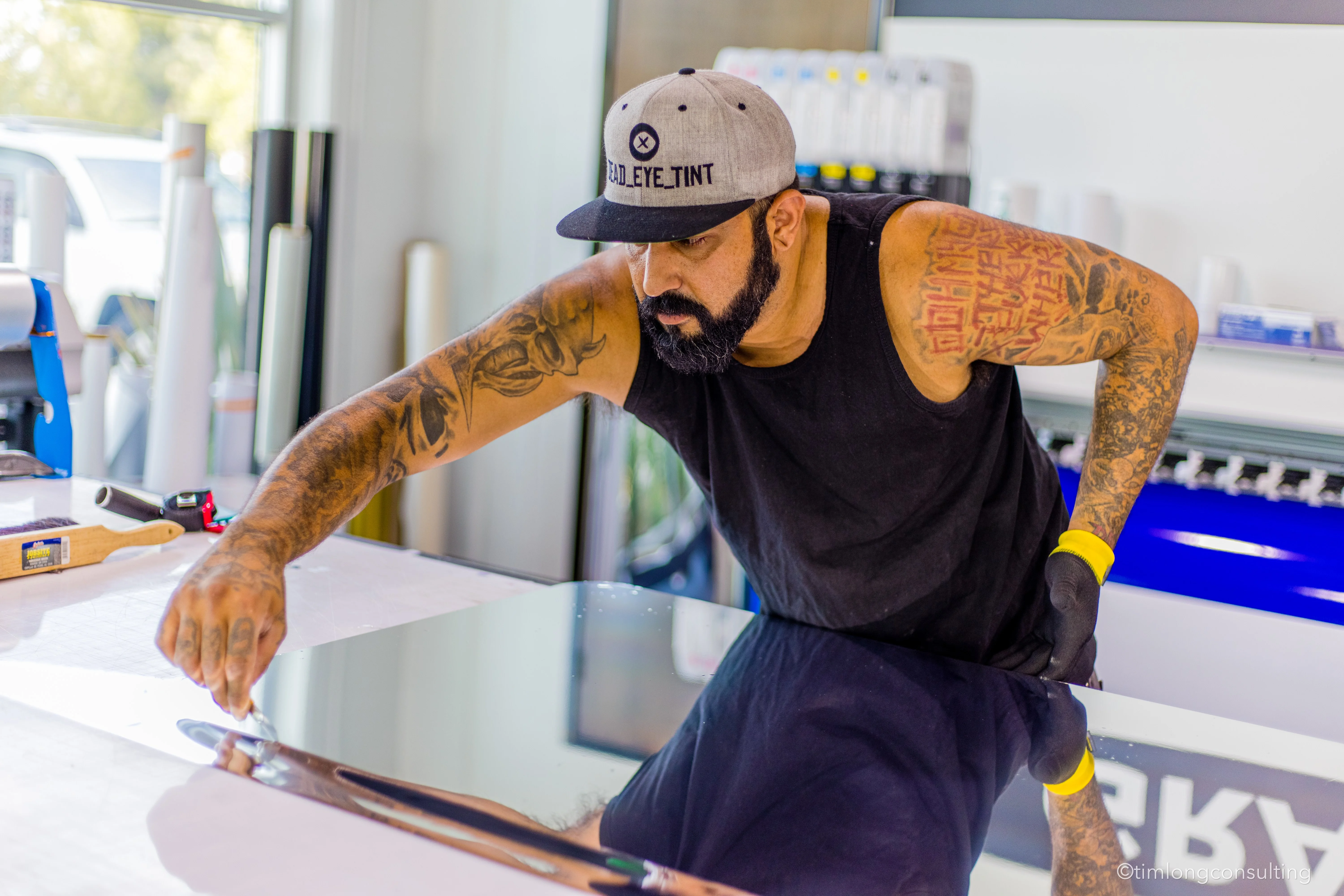 Professional tinting shop interior with precision application tools, finished vehicles, and display samples of ceramic films and vinyl wraps.